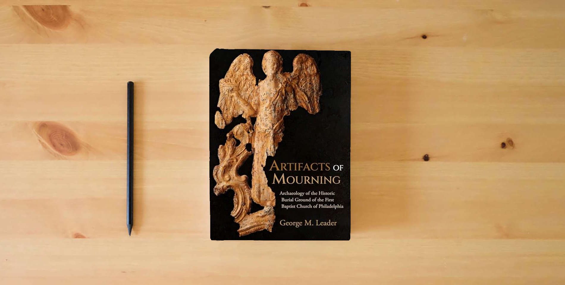 The book Artifacts of Mourning: Archaeology of the Historic Burial Ground of the First Baptist Church of Philadelphia (Studies in Funerary Archaeology) is on the table