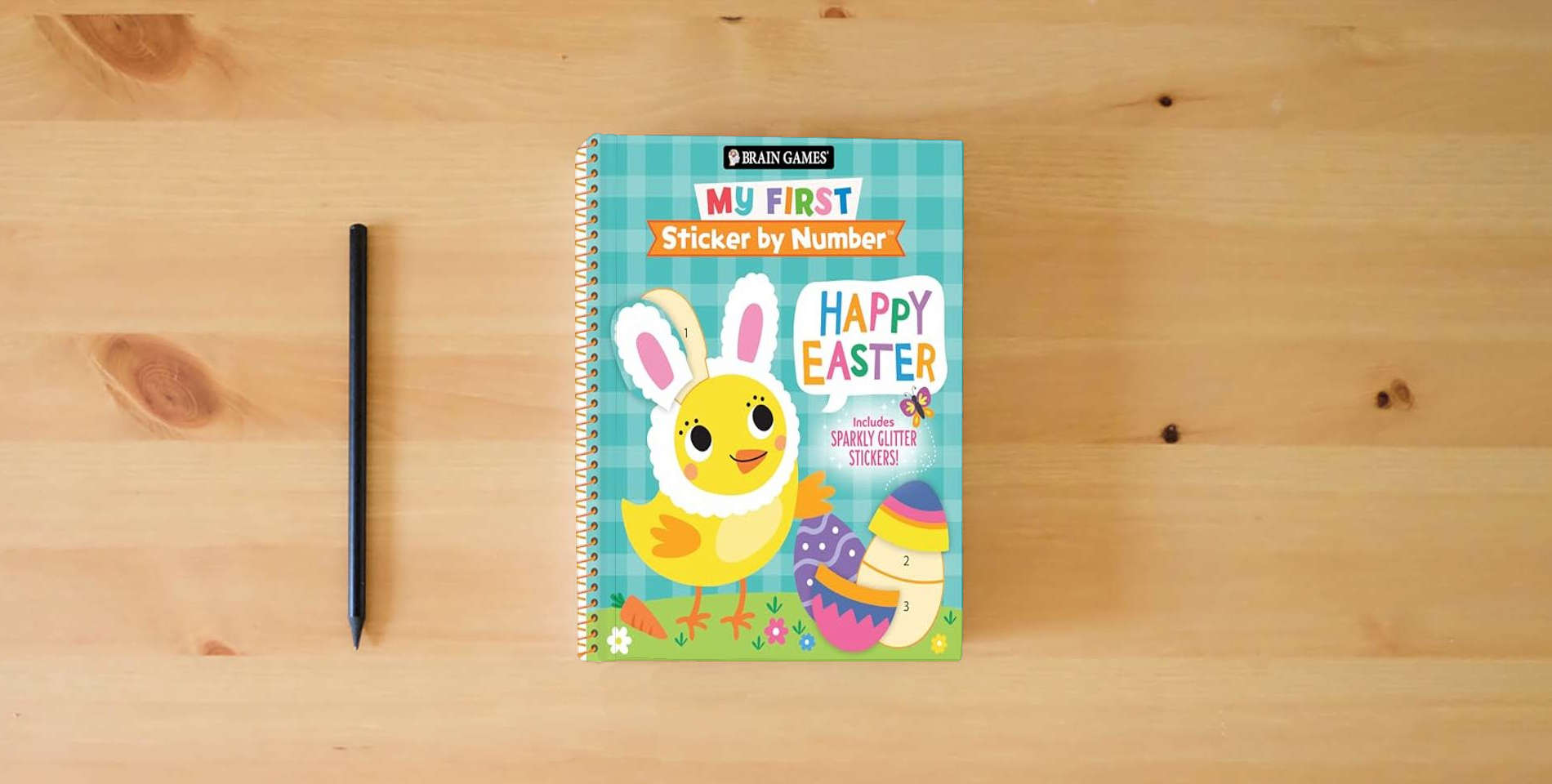 The book Brain Games - My First Sticker by Number: Happy Easter - Includes Sparkly Glitter Stickers! is on the table