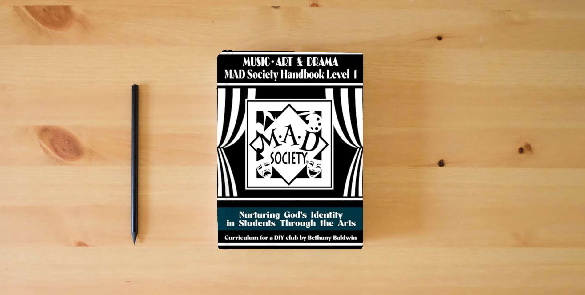 The book Music, Art & Drama MAD Society Handbook Level 1: Curriculum for a DIY Club to Nurture God's Identity in Students Through the Arts is on the table