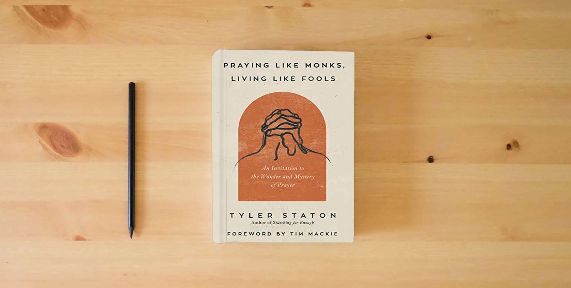 The book Praying Like Monks, Living Like Fools: An Invitation to the Wonder and Mystery of Prayer is on the table