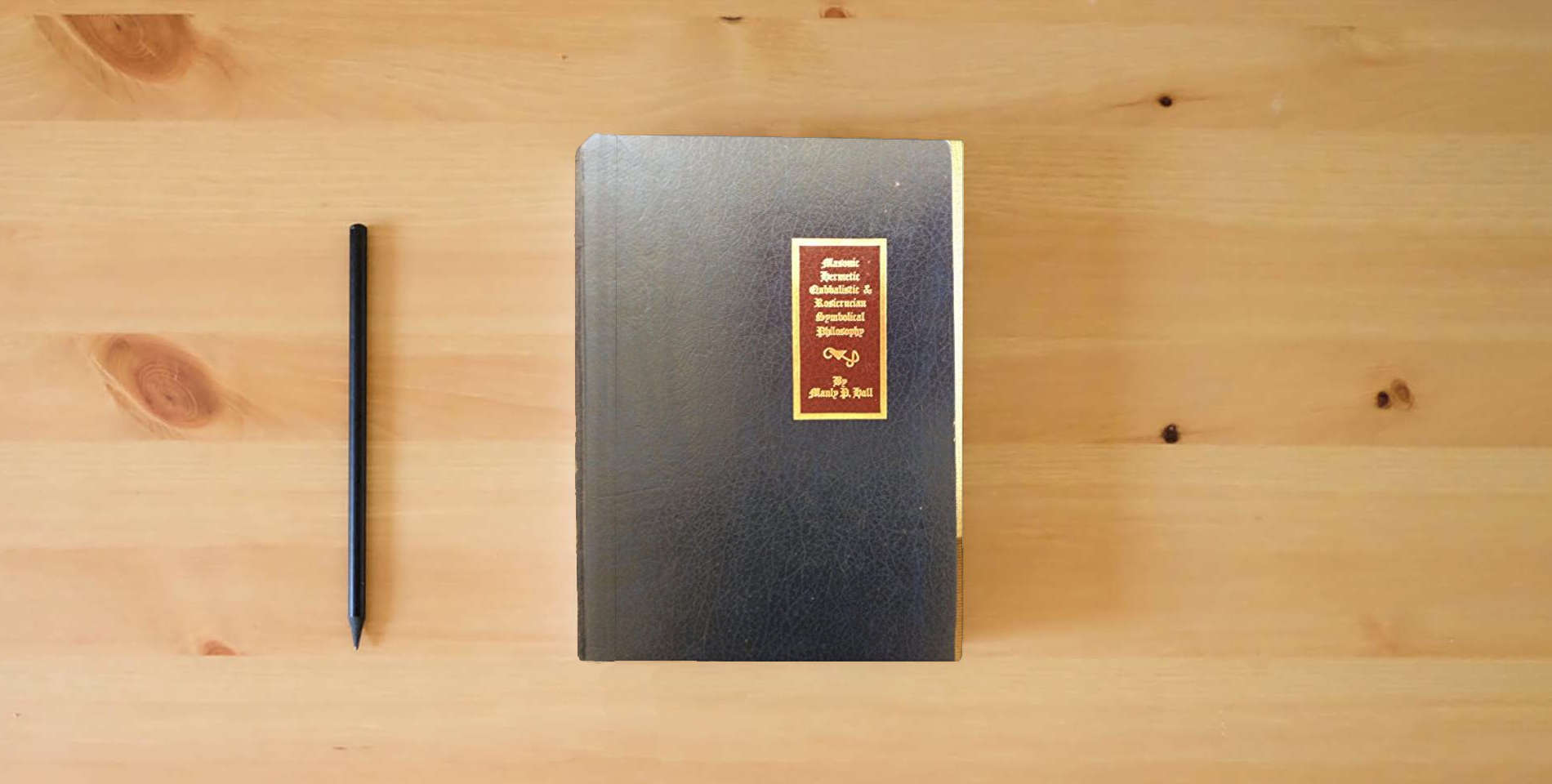 The book Secret Teachings of All Ages: An Encyclopedic Outline of Masonic, Hermetic, Qabbalistic and Rosicrucian Symbolical Philosophy (Golden Anniversary Edition) is on the table