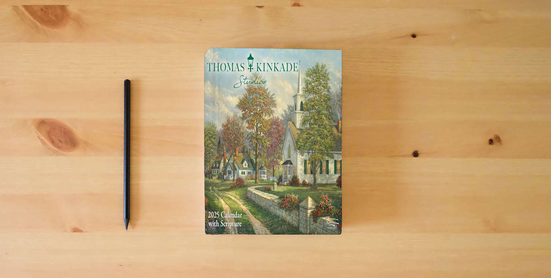 The book Thomas Kinkade Studios 2025 Deluxe Wall Calendar with Scripture is on the table