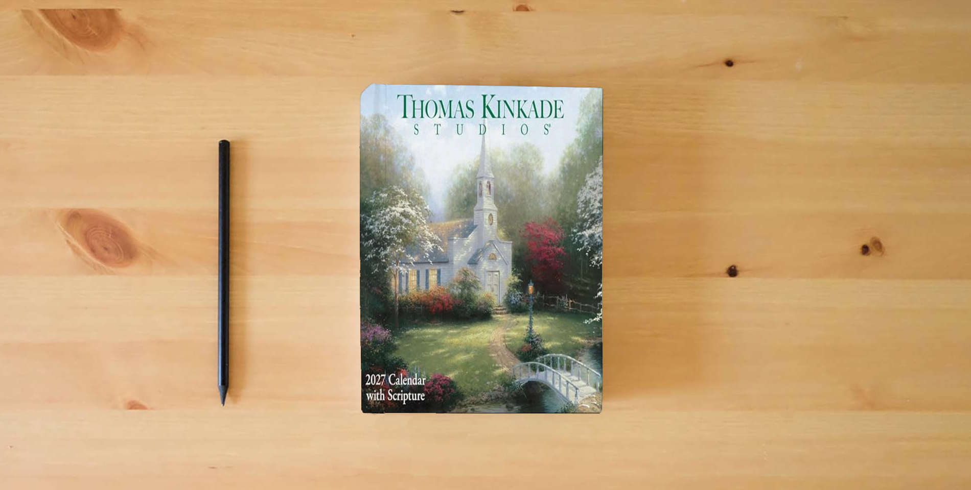 The book Thomas Kinkade Studios® 2027 Deluxe Wall Calendar with Scripture is on the table