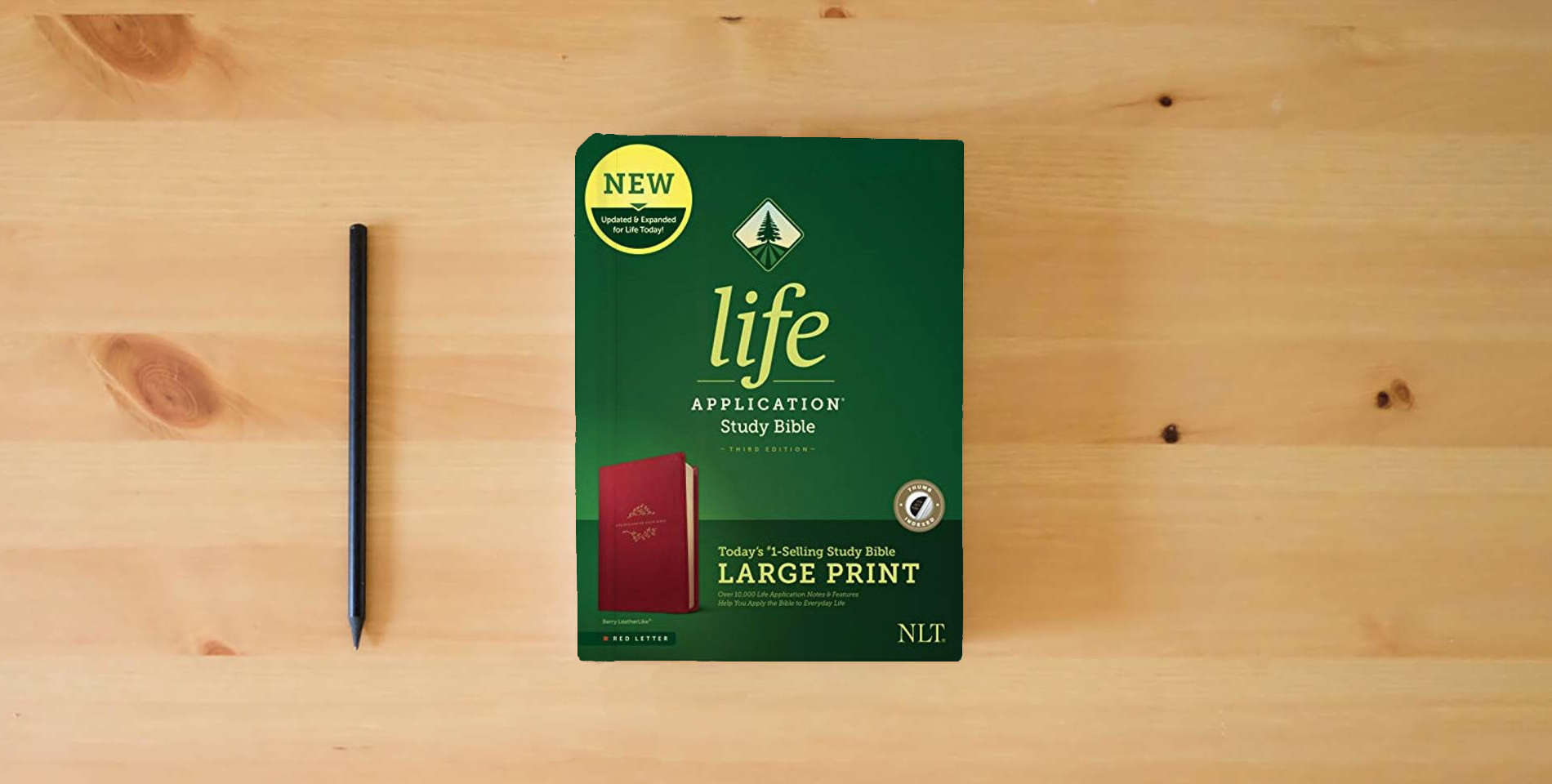 The book Tyndale NLT Life Application Study Bible, Third Edition, Large Print (LeatherLike, Berry, Indexed, Red Letter) – New Living Translation Bible, Large Print Study Bible for Enhanced Readability is on the table