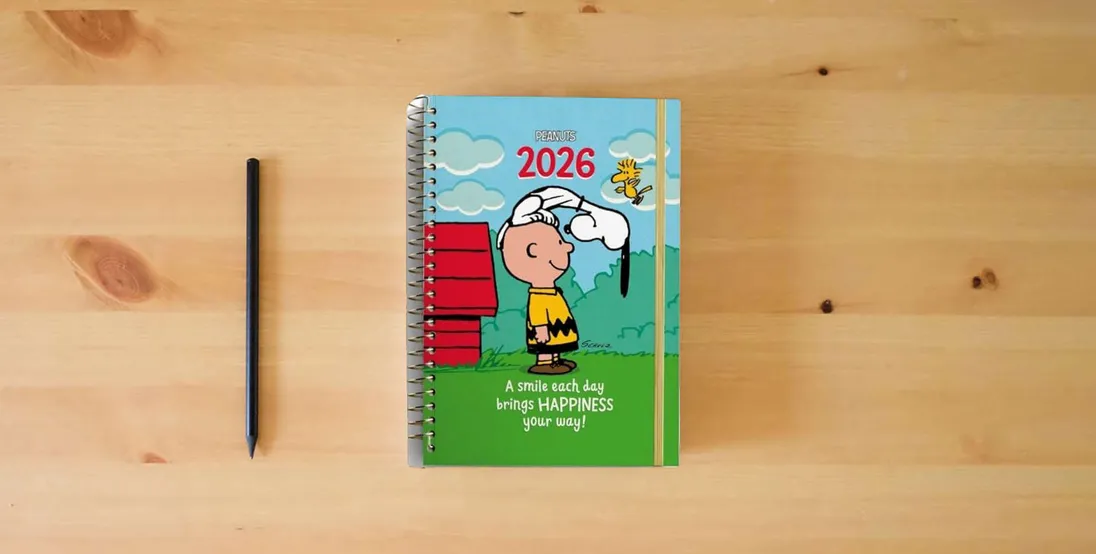 The book Peanuts A smile Each Day 2026 12-Month Inspirational Planner} is on the table