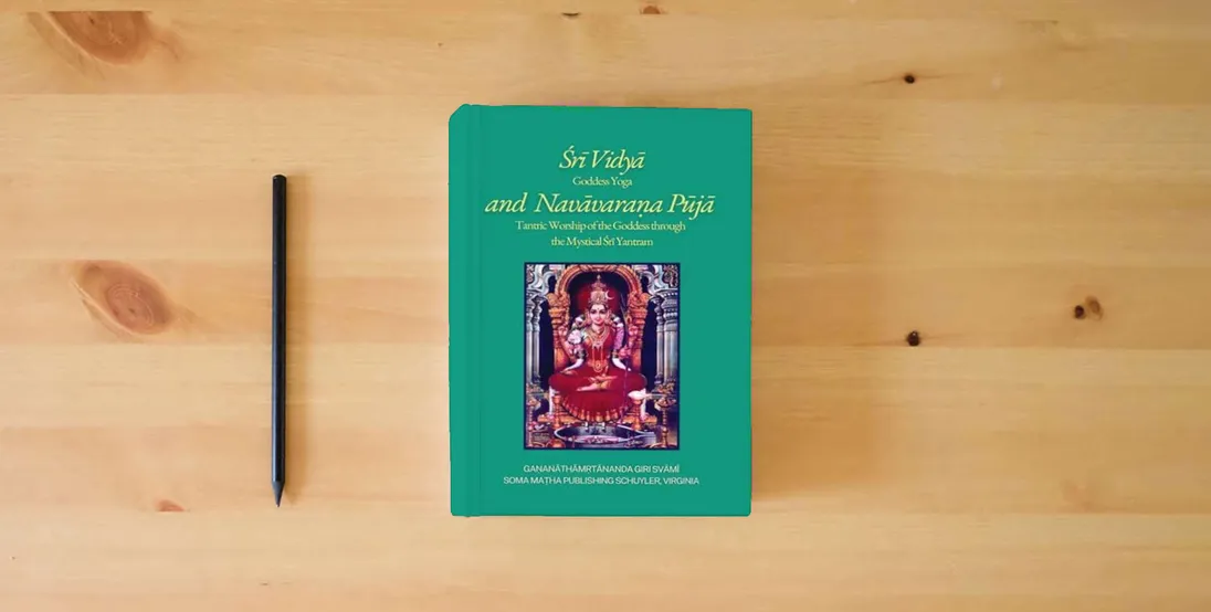 The book Śrī Vidyā and Navāvaraṇa Pūjā: Goddess Yoga and Tantric Worship of the Goddess through the Mystical Śrī Yantram} is on the table