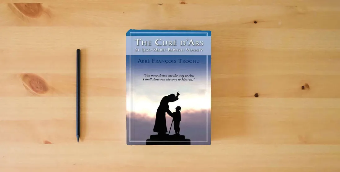 The book The Cure D'Ars : St. Jean-Marie-Baptiste Vianney} is on the table