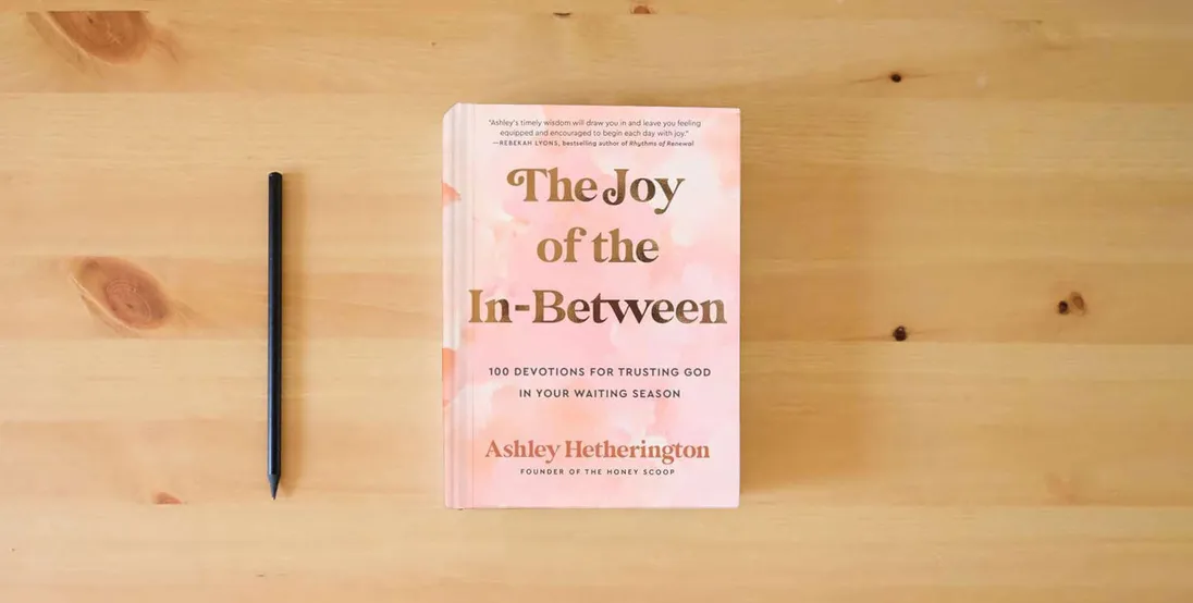 The book The Joy of the In-Between: 100 Devotions for Trusting God in Your Waiting Season: A Devotional} is on the table